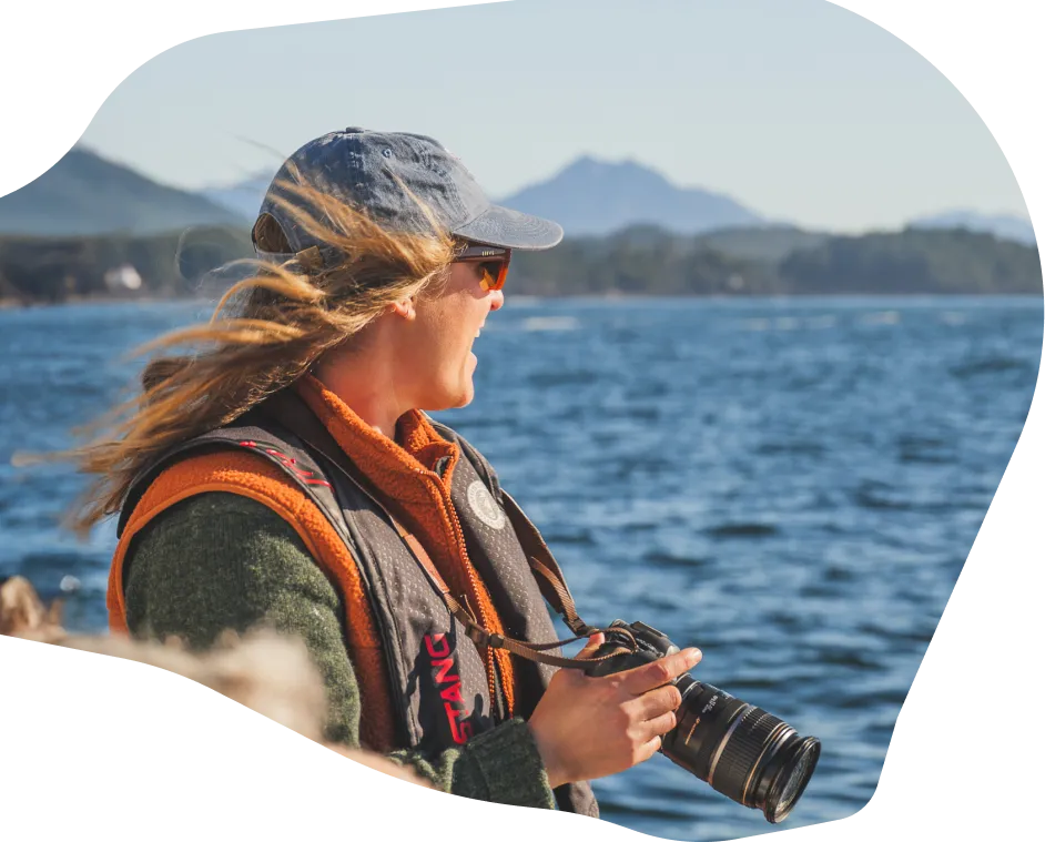 A woman overlooking the ocean holding a camera with a telephoto lens
