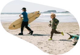 Two children on the beach, one carrying a surfboard