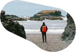 A man standing on the beach looking out on rock outcrops in the water