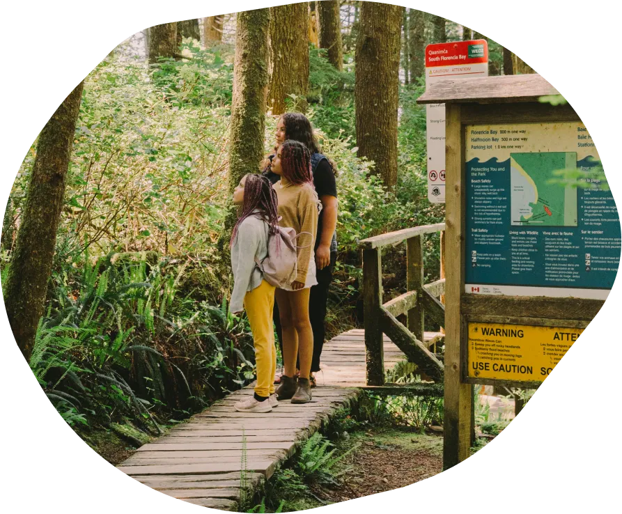 A family walking on a wooden boardwalk through a forest, next to park signage